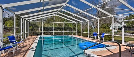 A covered swimming pool with clear blue water, surrounded by white metal beams and blue chairs.