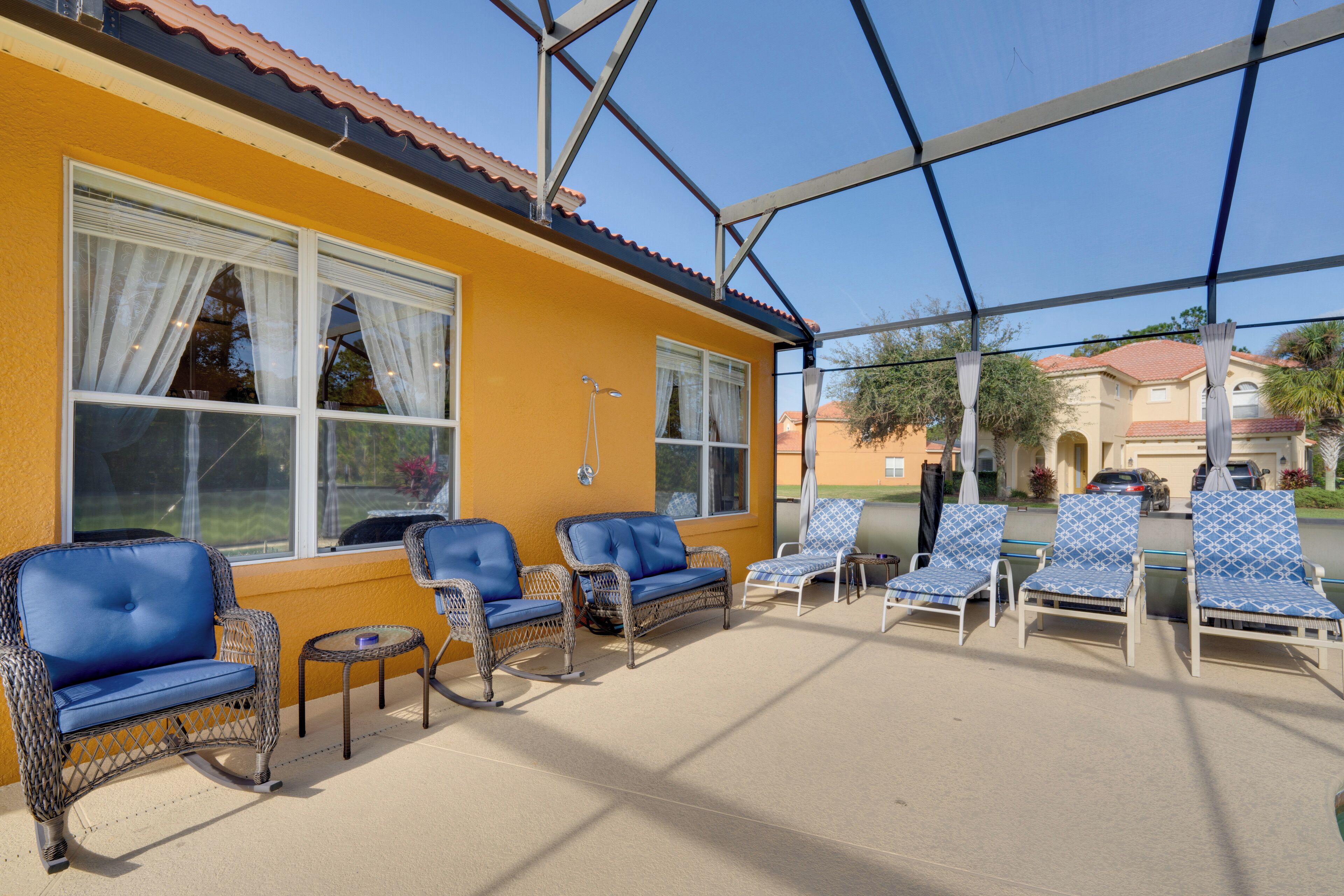 A covered outdoor seating area with wicker furniture and a yellow building in the background.