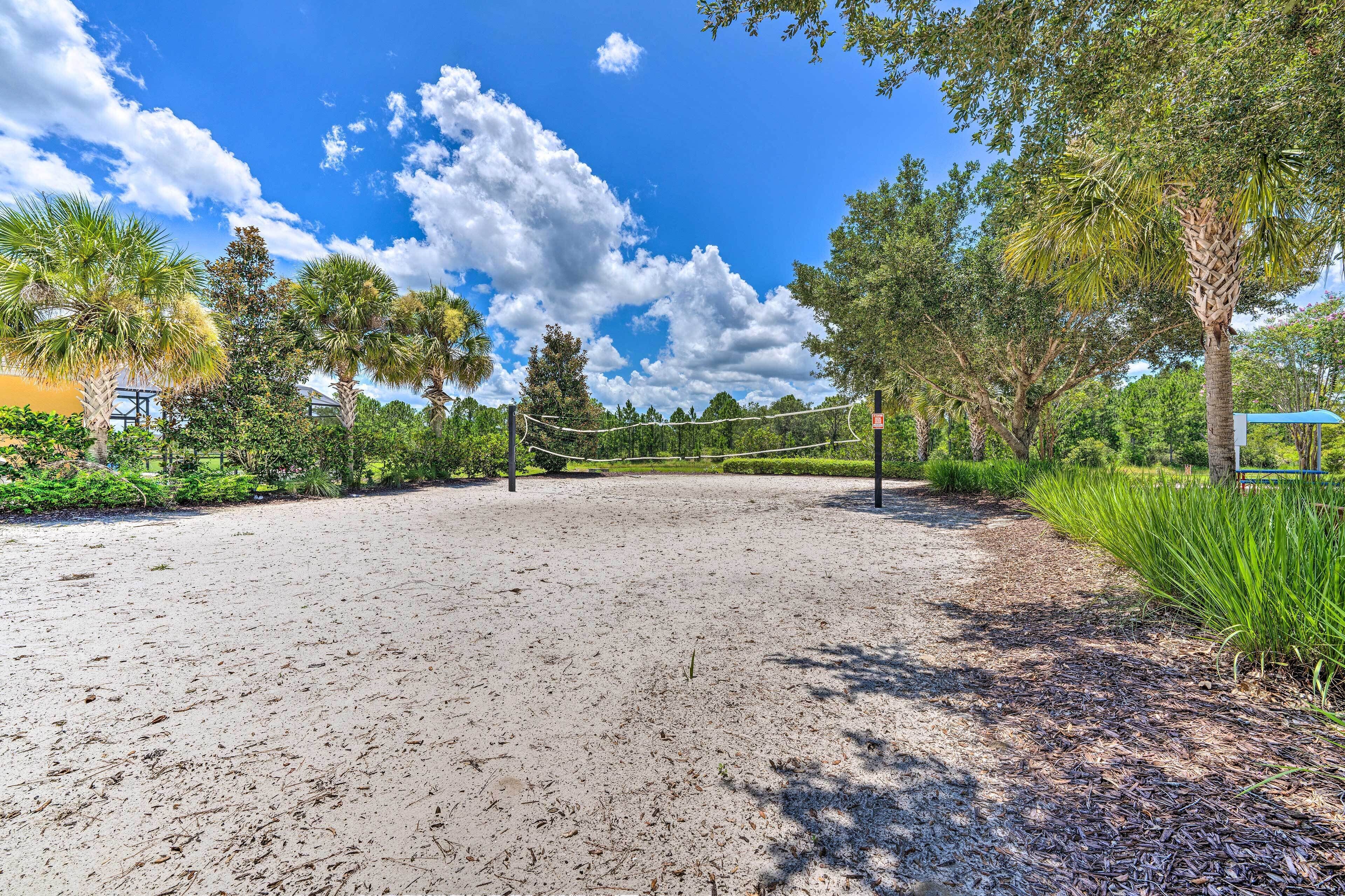 A sandy volleyball court surrounded by trees and greenery, with a clear blue sky above.