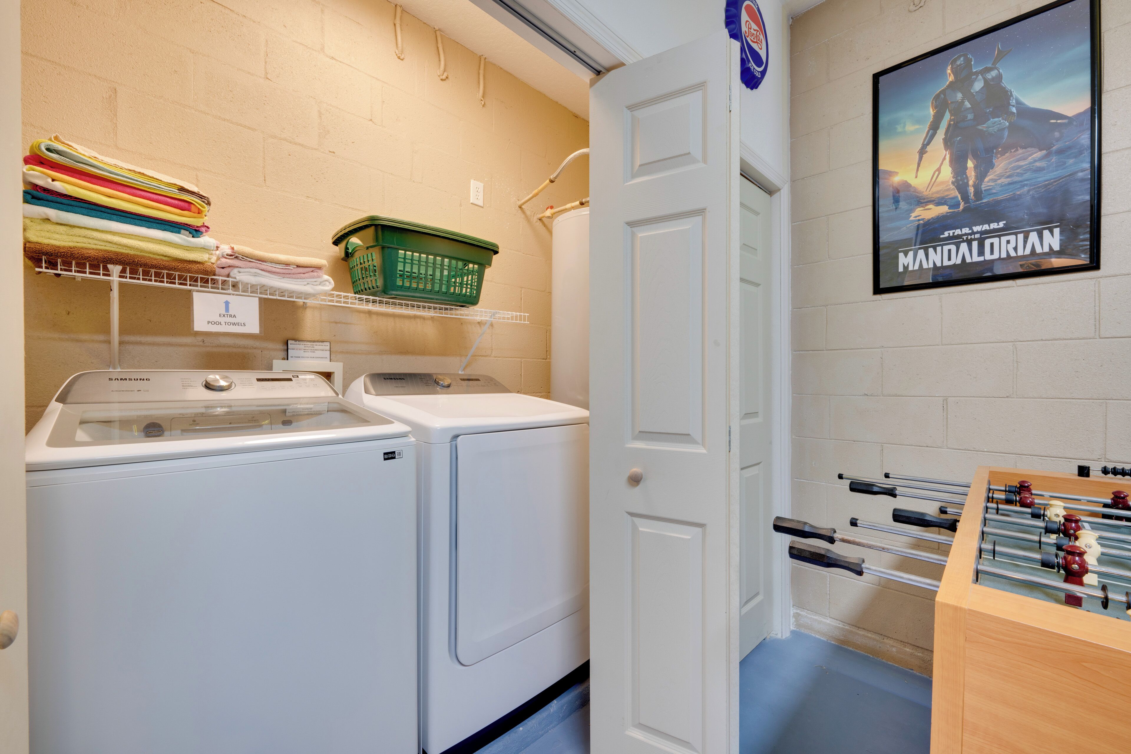 A laundry area with stacked towels, a green basket, and a Samsung washing machine.