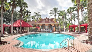 Une piscine entourée de palmiers, avec des chaises longues et des parasols, et un bâtiment doté d’un toit rouge.