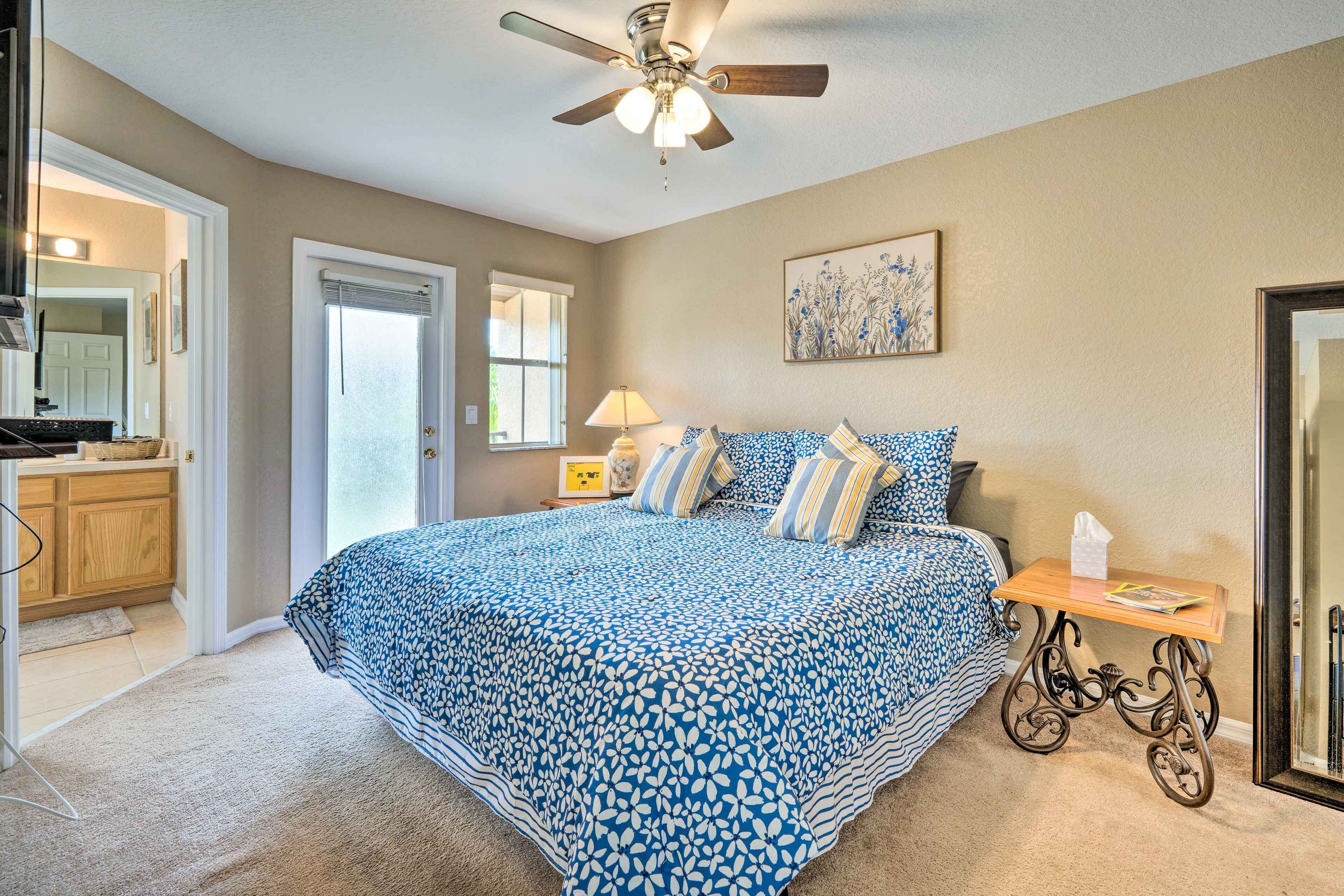 A bedroom with a large bed, a ceiling fan, a bedside table with a lamp, and a door leading to a bathroom.