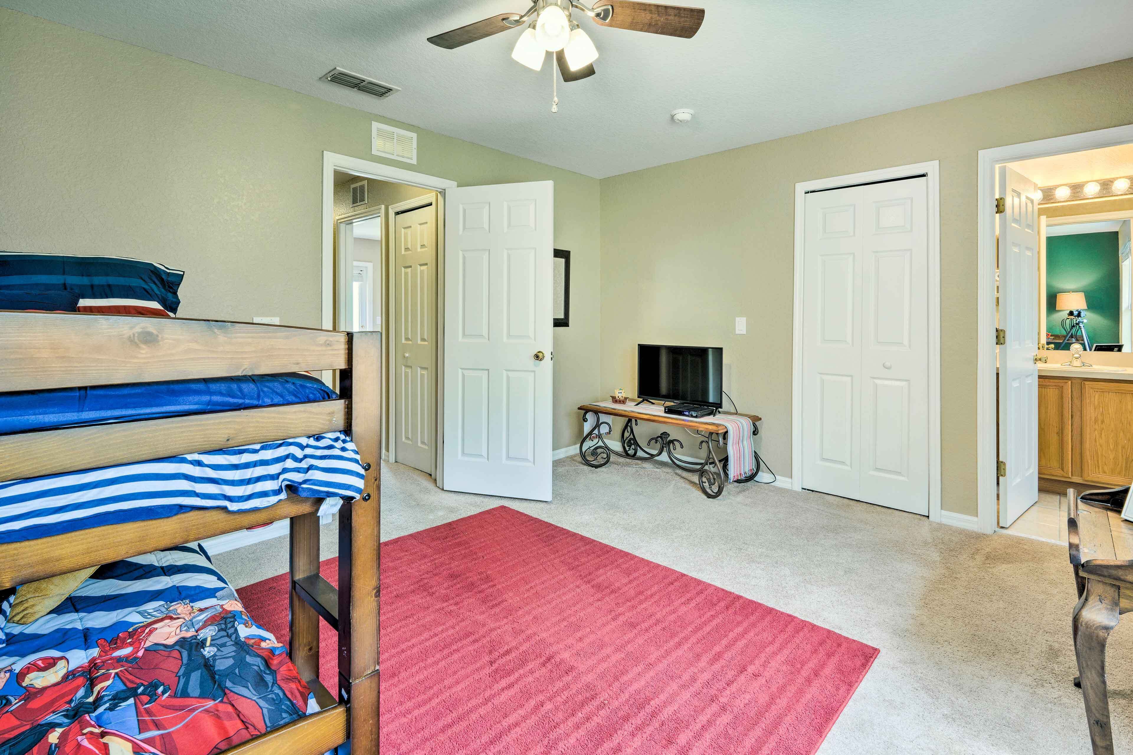 A bedroom with bunk beds, a red carpet, a ceiling fan, a TV, and a vanity with a mirror.