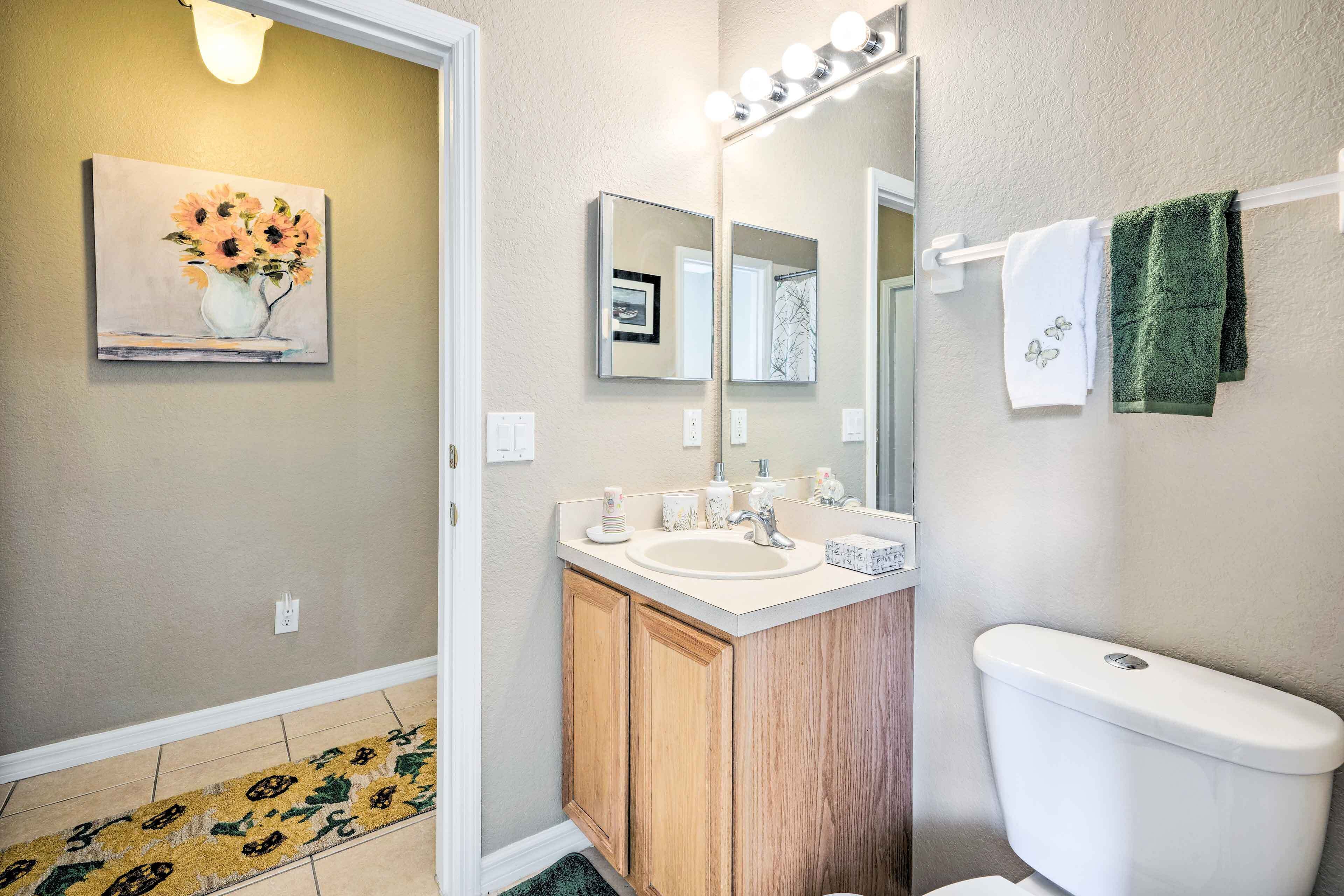 A bathroom with a sink, mirror, and toilet. There is a painting on the wall and a towel rack with towels.