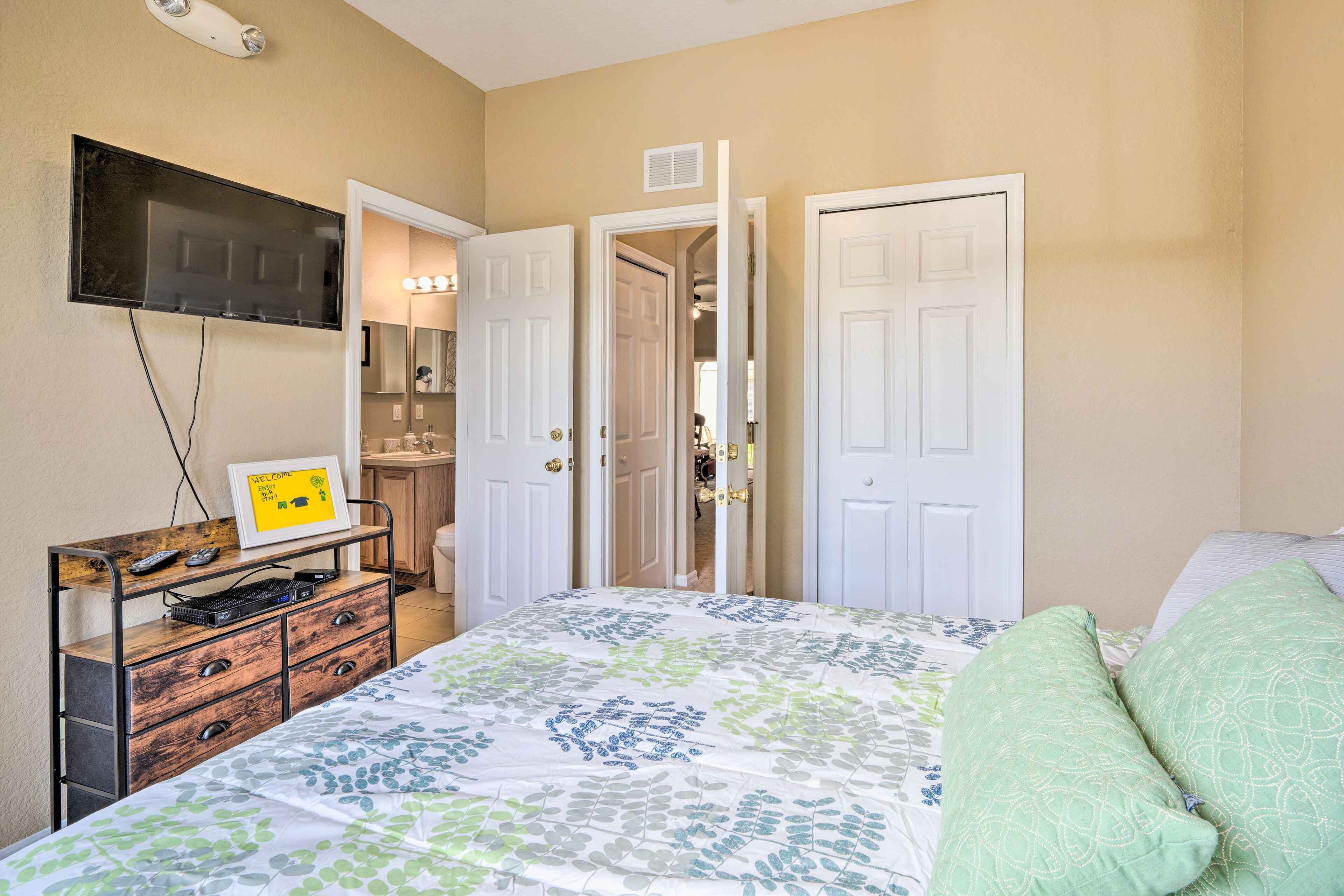 Un dormitorio con cama, cómoda, televisor y puerta que da a un baño.