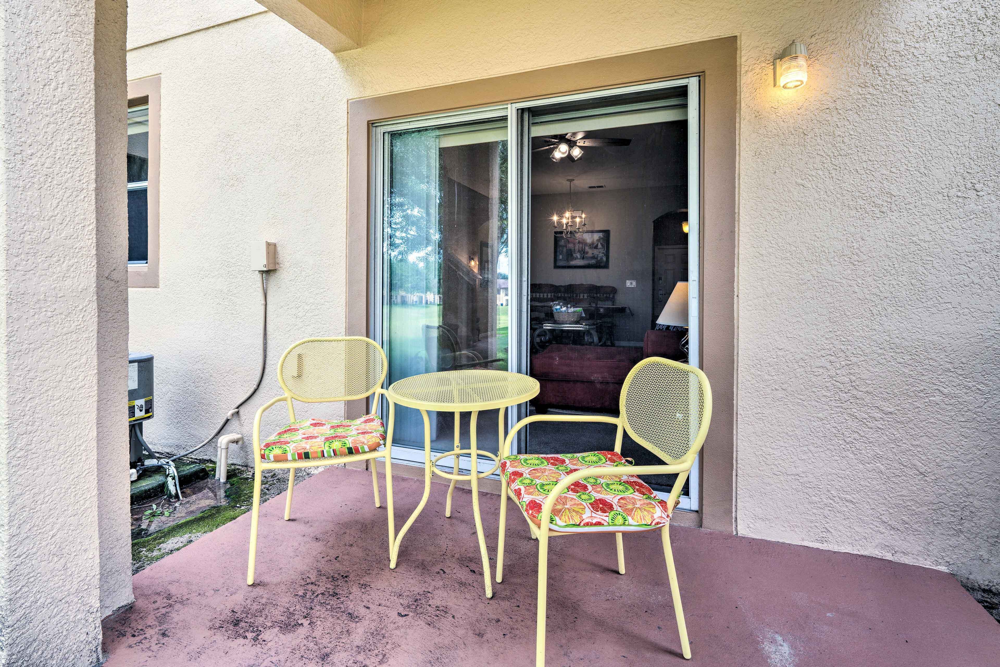 Eine Terrasse mit zwei gelben Stühlen und einem kleinen Tisch, eine Glasschiebetür, die zu einem Innenraum führt, sowie eine wandmontierte Leuchte.