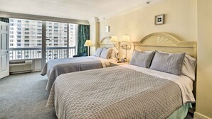 A hotel room with two beds, a window with a view of buildings, a bedside table with lamps, and a wall clock. - Sunny Daytona Beach Gem w/ Ocean Views! (Daytona Beach)