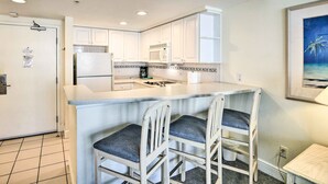 A kitchen with white cabinets, a microwave, a refrigerator, and a bar area with two chairs. - Sunny Daytona Beach Gem w/ Ocean Views! (Daytona Beach)