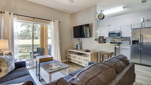 Una sala moderna con sofá, mesa de centro y televisor. Hay una zona de cocina con microondas y refrigerador.