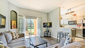 A modern living room with a sofa, a coffee table, and a TV. There is a kitchen area with a microwave and a bar. - 9 Mi to Disney: Davenport Townhome w/ Resort Pool! (Davenport)