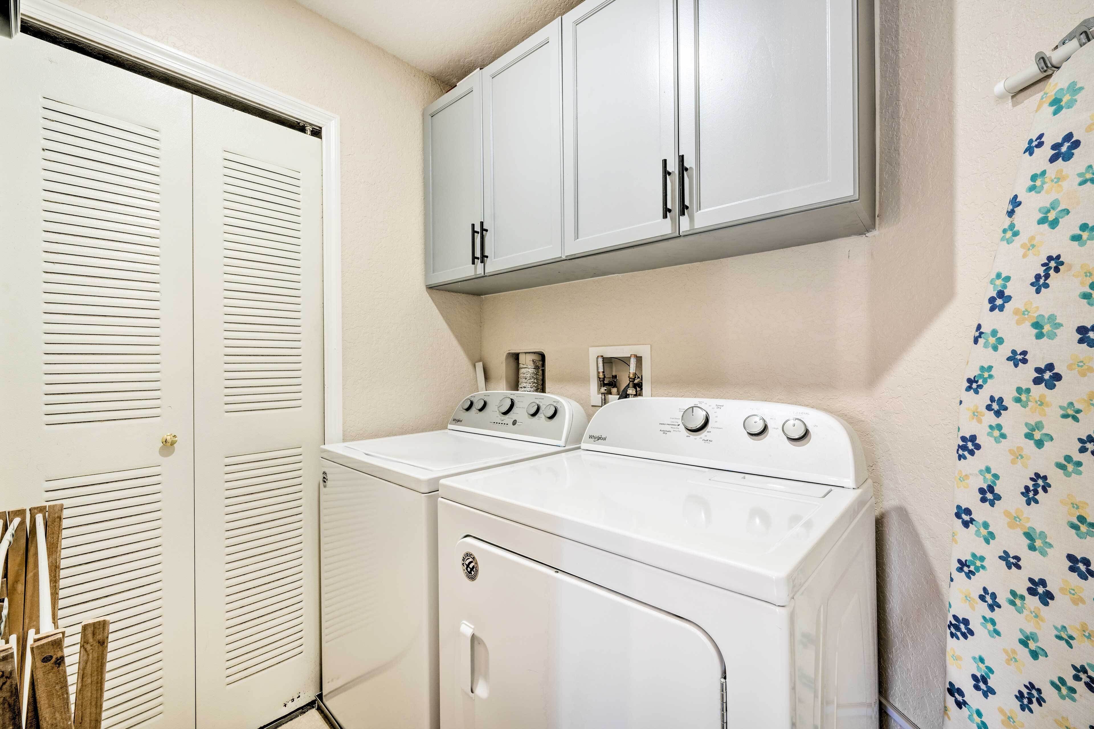 A laundry room with a front-loading washer and dryer, a white cabinet above, and a shower curtain with a floral pattern.