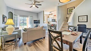 A modern living room with a sofa, a dining table, and chairs. There is a ceiling fan, a lamp, and a staircase leading to an upper level. - 9 Mi to Disney: Davenport Townhome w/ Resort Pool! (Davenport)