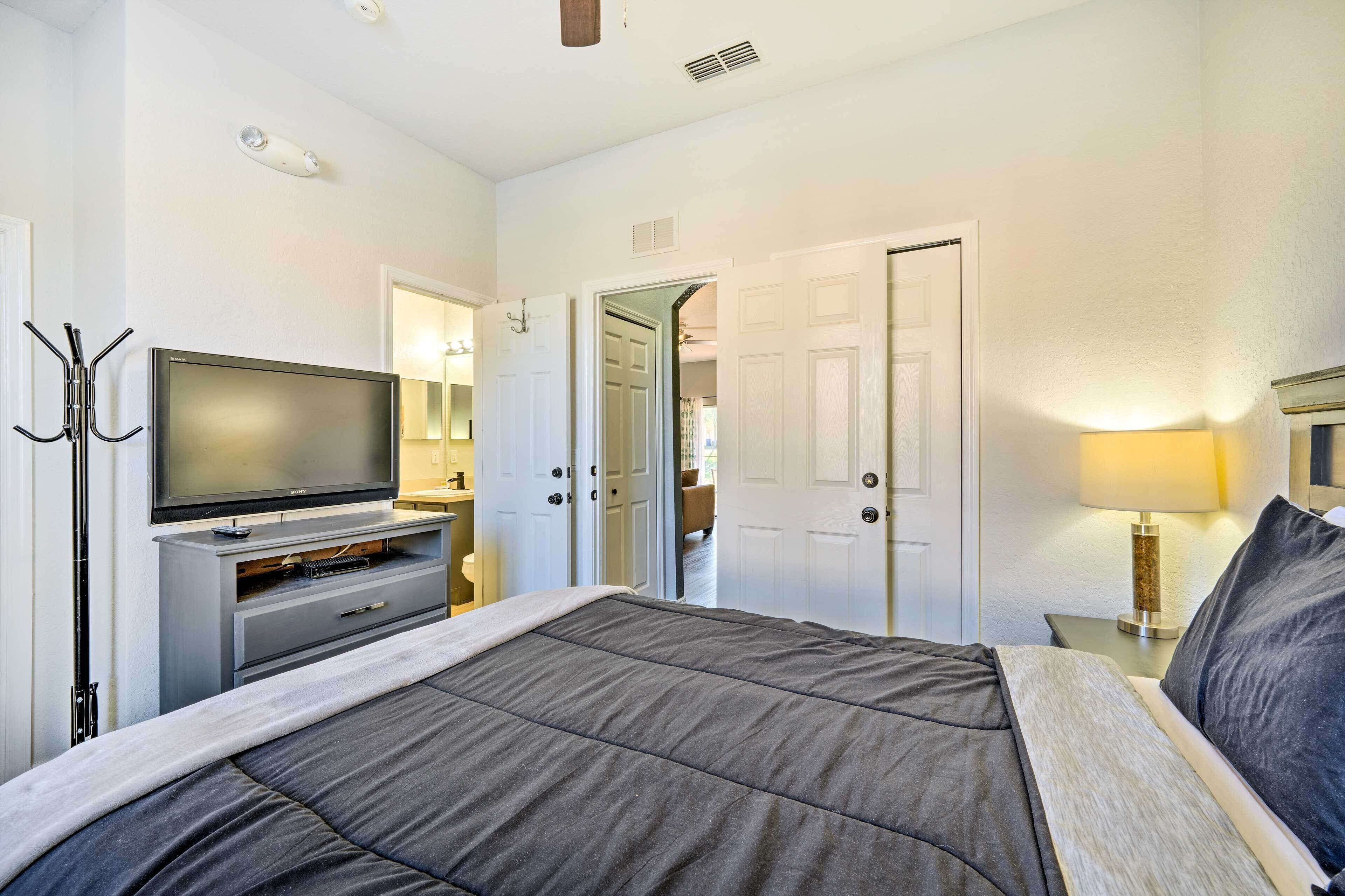 A hotel room with a bed, a TV, a desk with a lamp, and a coat rack.