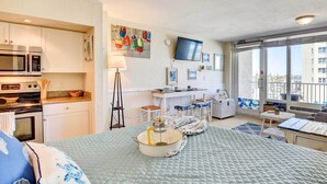 A compact hotel room with a kitchenette, a bed, a desk, and a balcony with a view. - Daytona Beach Studio With Balcony + Ocean View (Daytona Beach Shores)