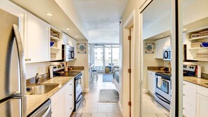 A narrow kitchen with white cabinets, stainless steel appliances, and a view to a balcony. - Daytona Beach Studio With Balcony + Ocean View (Daytona Beach Shores)
