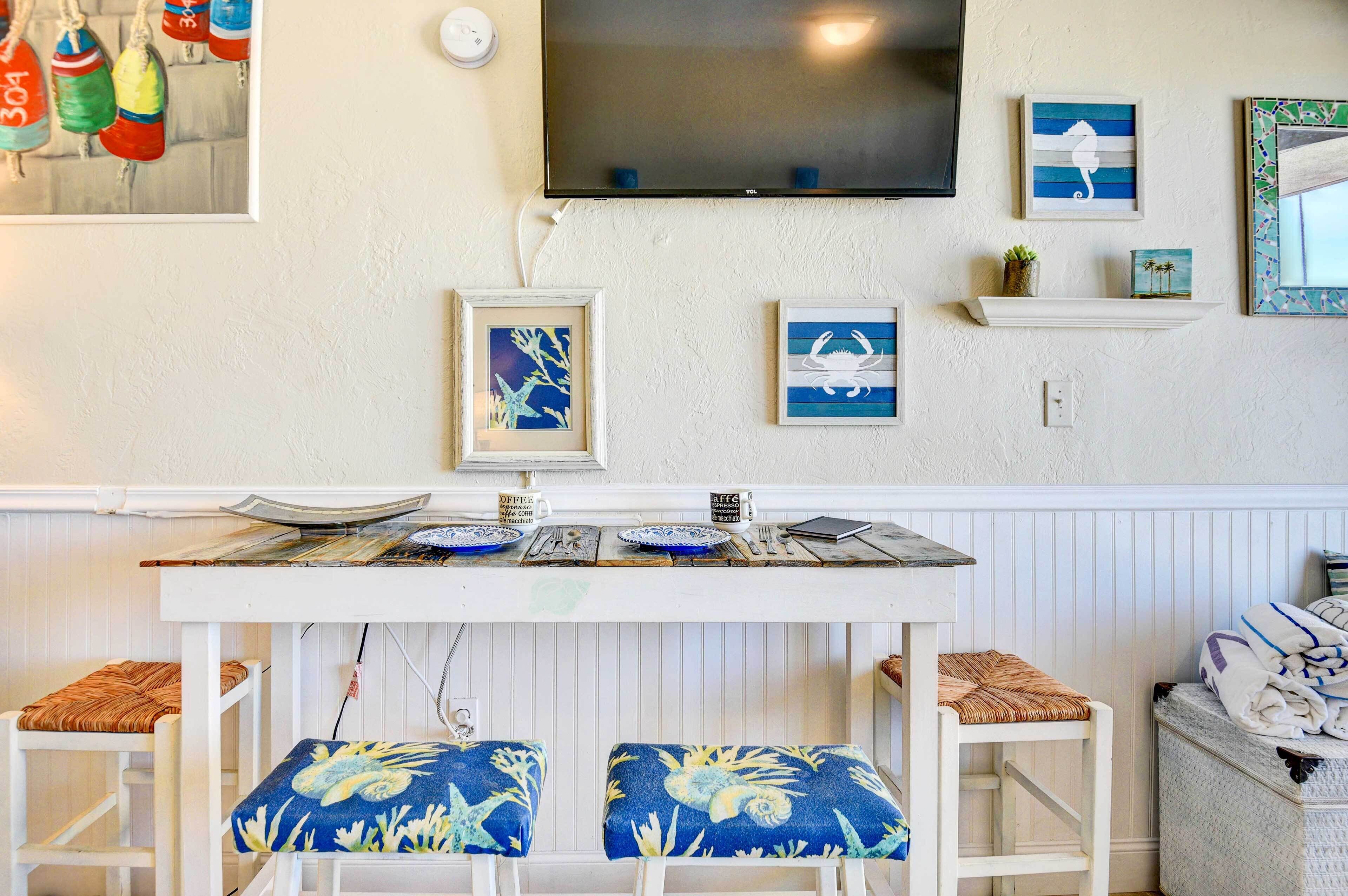 A dining area with a white table, blue patterned cushions, and a flat-screen TV mounted on the wall.