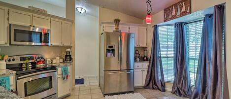 A modern kitchen with stainless steel appliances, white cabinets, and a large window with curtains.