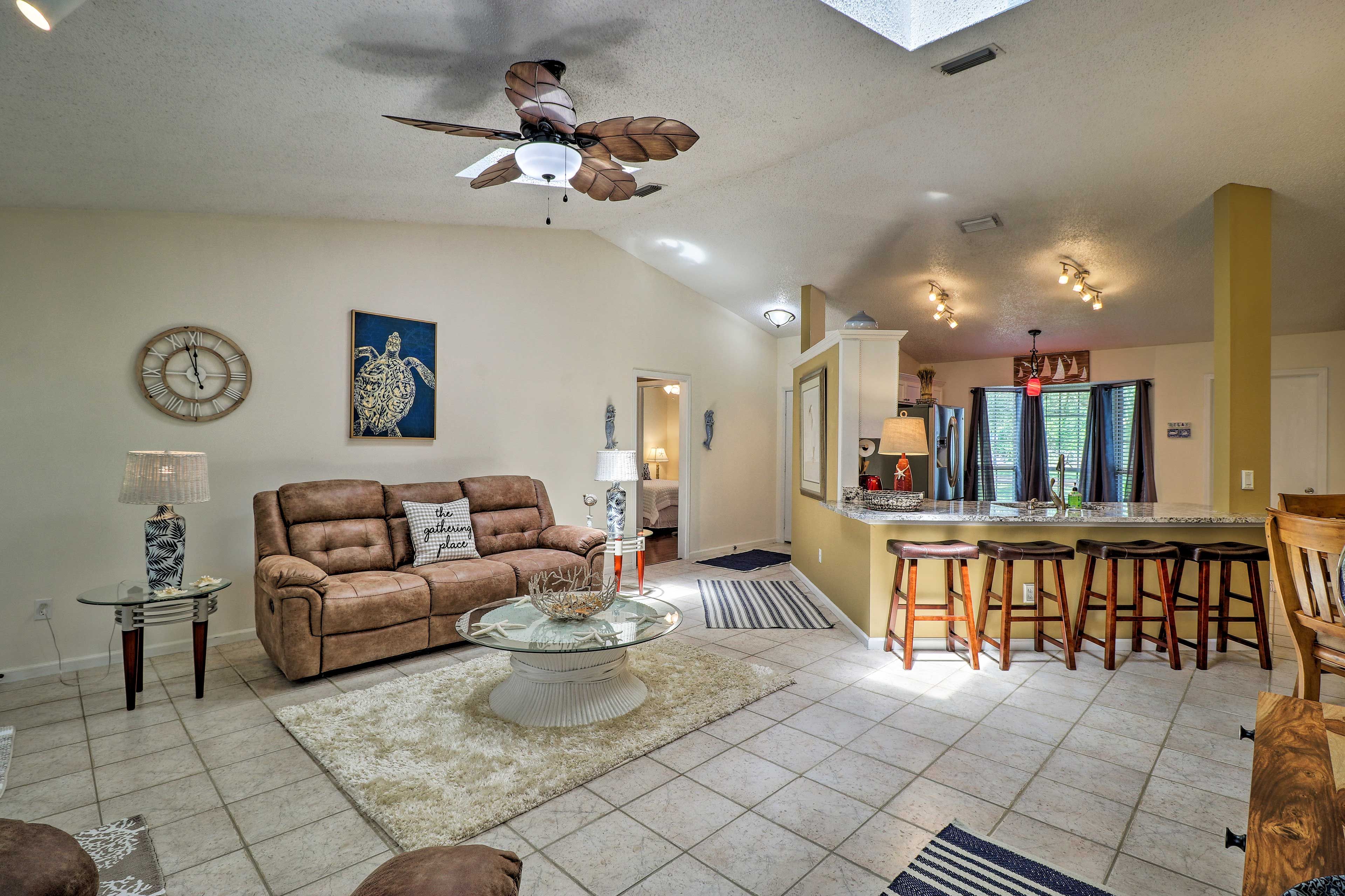 A living room with a brown leather couch, a glass coffee table, and a ceiling fan.