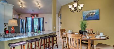 A kitchen with a central island, bar stools, a dining table with chairs, and a chandelier.