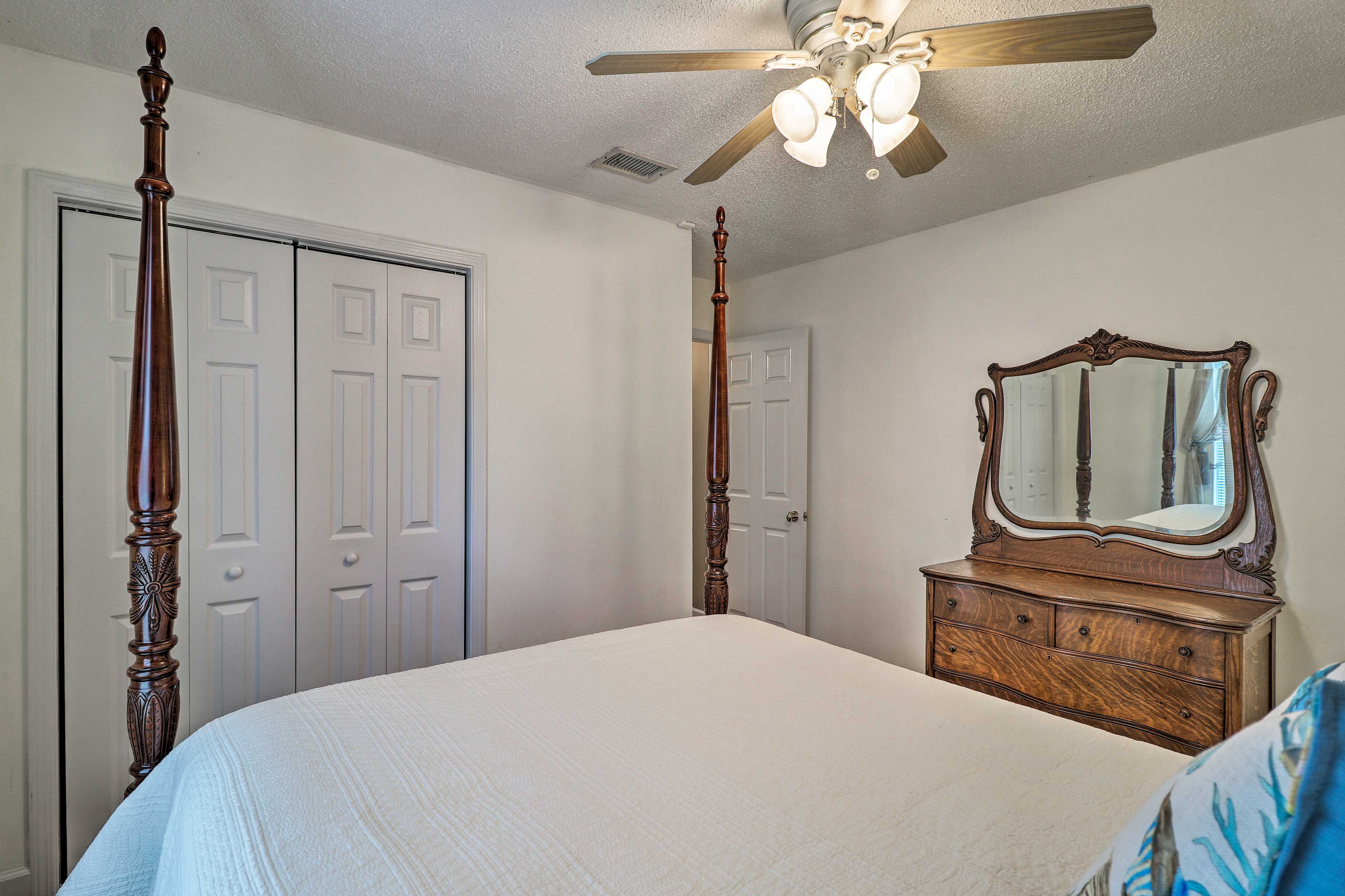 A bedroom with a four-poster bed, a dresser with a mirror, and a ceiling fan.