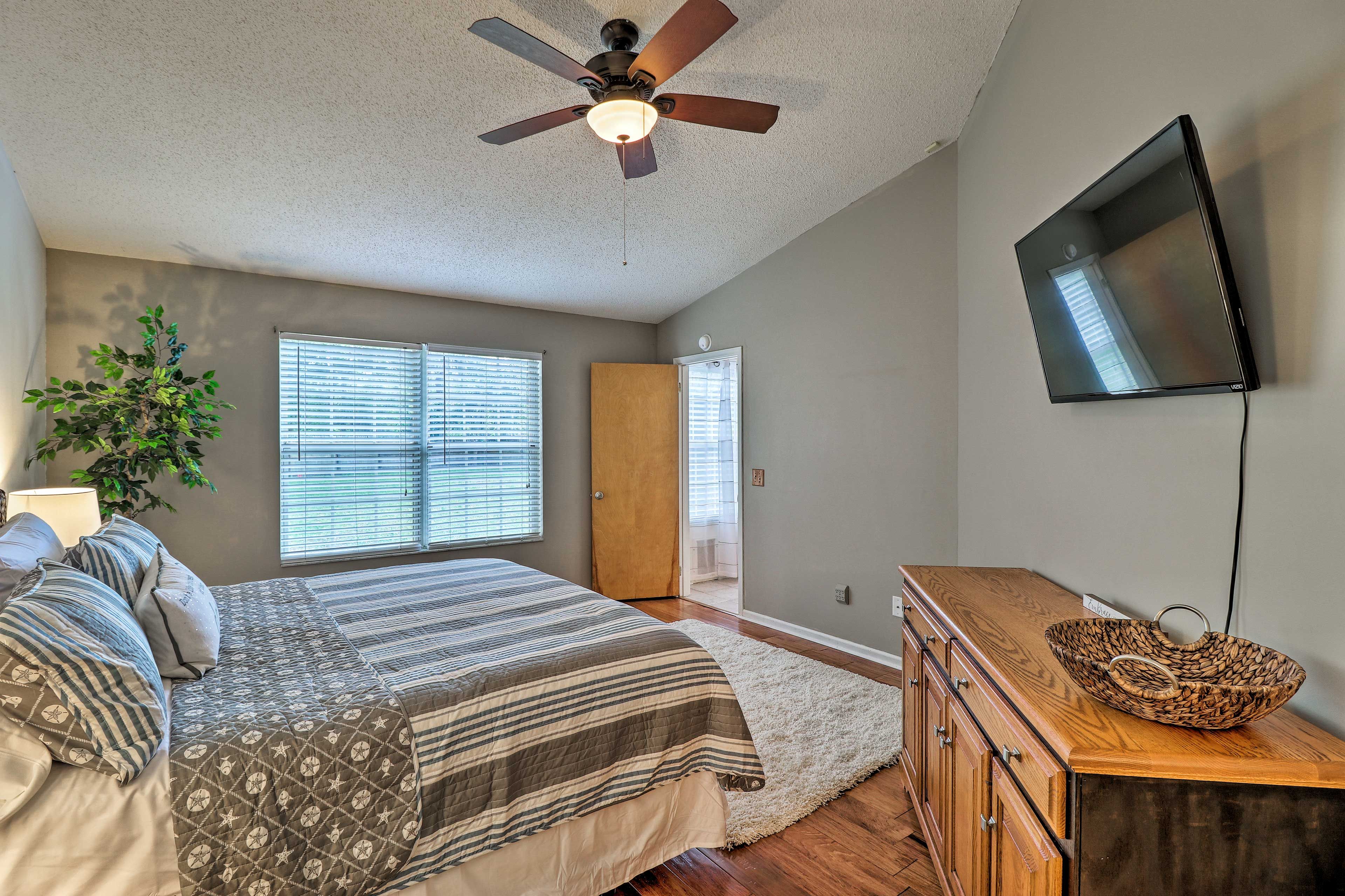 Une chambre à coucher avec un lit, un ventilateur de plafond, un téléviseur fixé au mur et une commode en bois.