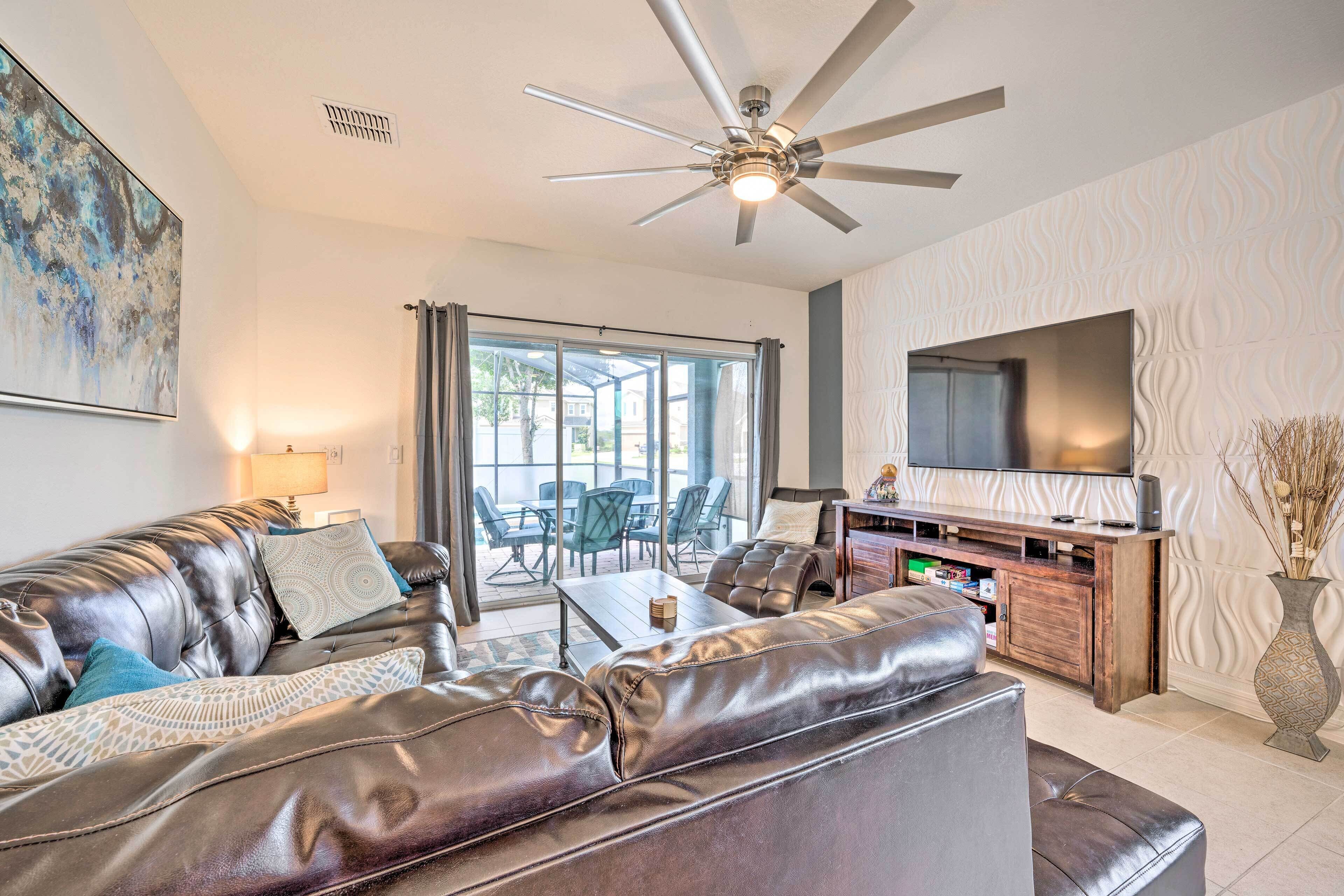 A modern living room with leather sofas, a flat-screen TV, and a ceiling fan.