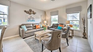 Un salon avec un canapé en cuir marron, deux fauteuils, une table basse et un tapis. On y trouve également des éléments décoratifs accrochés au mur et une fenêtre donnant sur l’extérieur.
