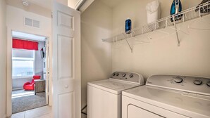 Une buanderie équipée de deux machines à laver et deux sèche-linge superposés, d’un étendoir et d’une chaise rouge dans la pièce adjacente.