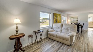 A living room with a beige sofa, a lamp, a small side table, and a window with a view of the outside.