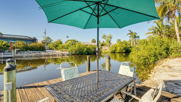A wooden deck with a table and chairs, a green umbrella, and a calm water body with reflections.