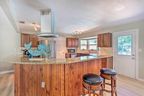 A kitchen with a wooden island, bar stools, a microwave, and a refrigerator.