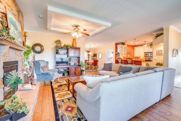 A spacious living room with a fireplace, a large grey sectional sofa, a wooden coffee table, and a variety of decorative plants.