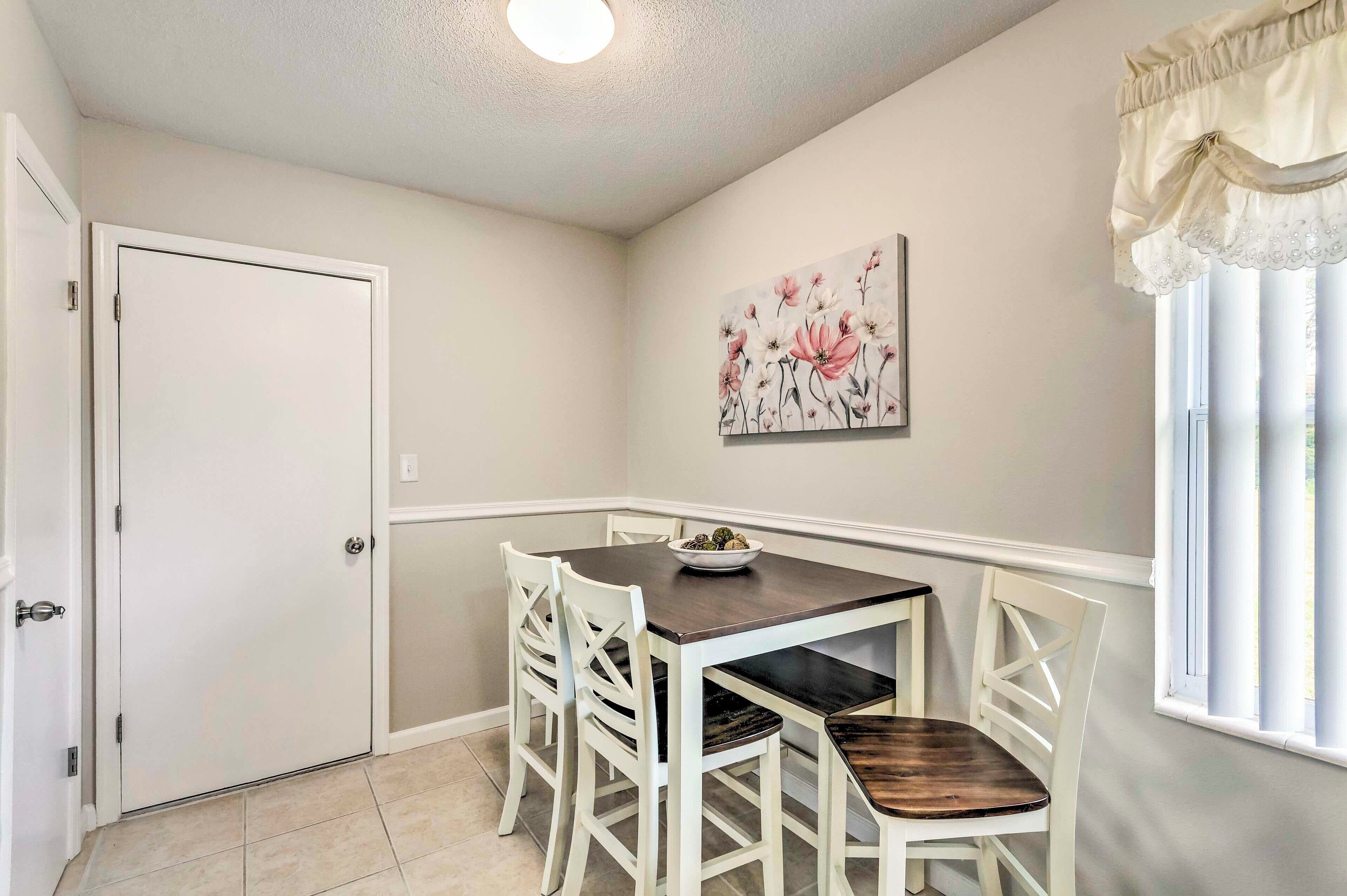 A dining area with a table and four chairs, a door, and a window with curtains.