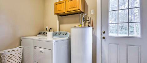 Een wasruimte met een wasmachine en droger, een hoge boiler, houten kasten en een deur met een raam.