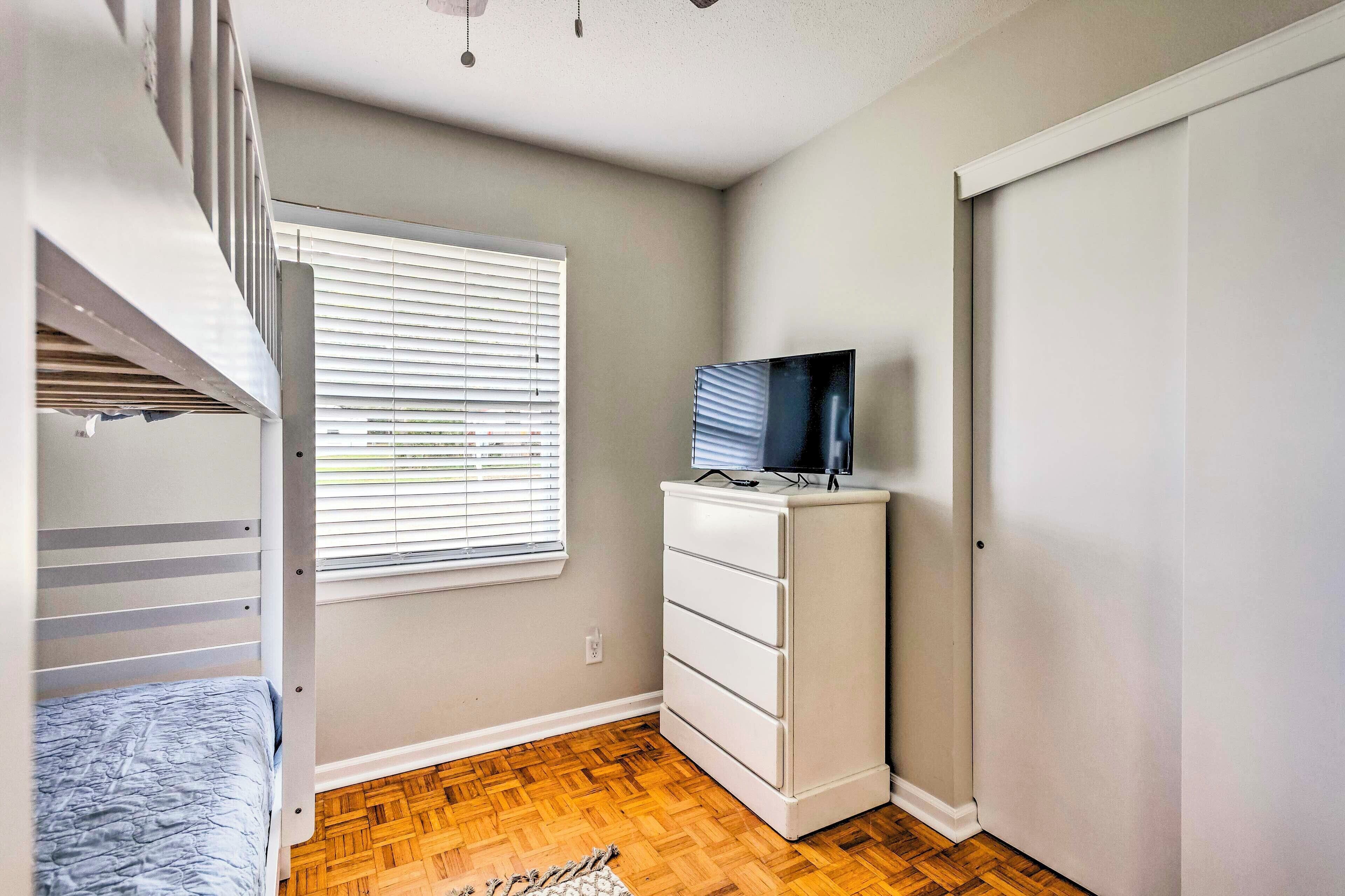 Ein Schlafzimmer mit Etagenbett, Kommode, Fernseher und Fenster mit Jalousien.