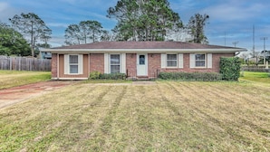 A single-story brick house with a front porch, a small front yard, and a wooden fence.