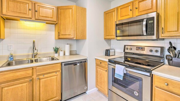 A kitchen with wooden cabinets, stainless steel appliances including a dishwasher, microwave, and oven, a sink, and a countertop with a toaster.