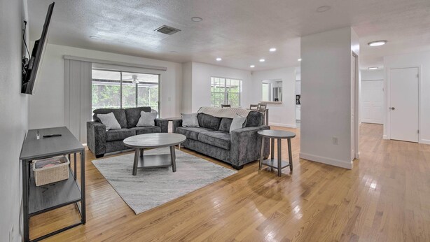 A spacious living room with hardwood flooring, grey sofas, a coffee table, and a TV mounted on the wall. - Family-friendly Ocala Retreat: 18 Mi to Dtwn! (Ocala)