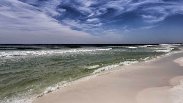 Ein Strand mit Wellen, blauem Himmel und Horizont.