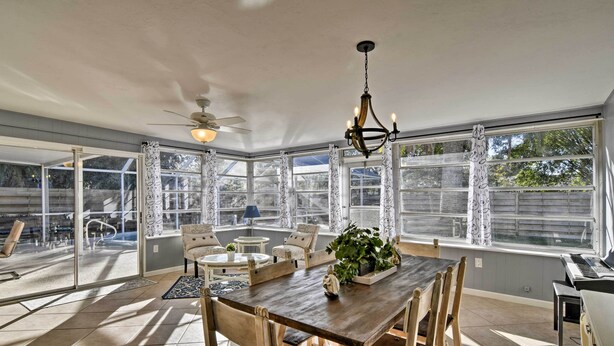 A spacious dining area with a large table and chairs, a chandelier, and large windows offering views of the outdoors. - Florida Home 3 Mi to Siesta Key, Walk to Gulf Gate (Sarasota)