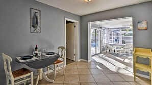 A dining area with a table set for two, a wine bottle, and glasses. There is a chair with a woven seat cushion. The room has a gray wall and a ceiling light fixture. - Florida Home 3 Mi to Siesta Key, Walk to Gulf Gate (Sarasota)