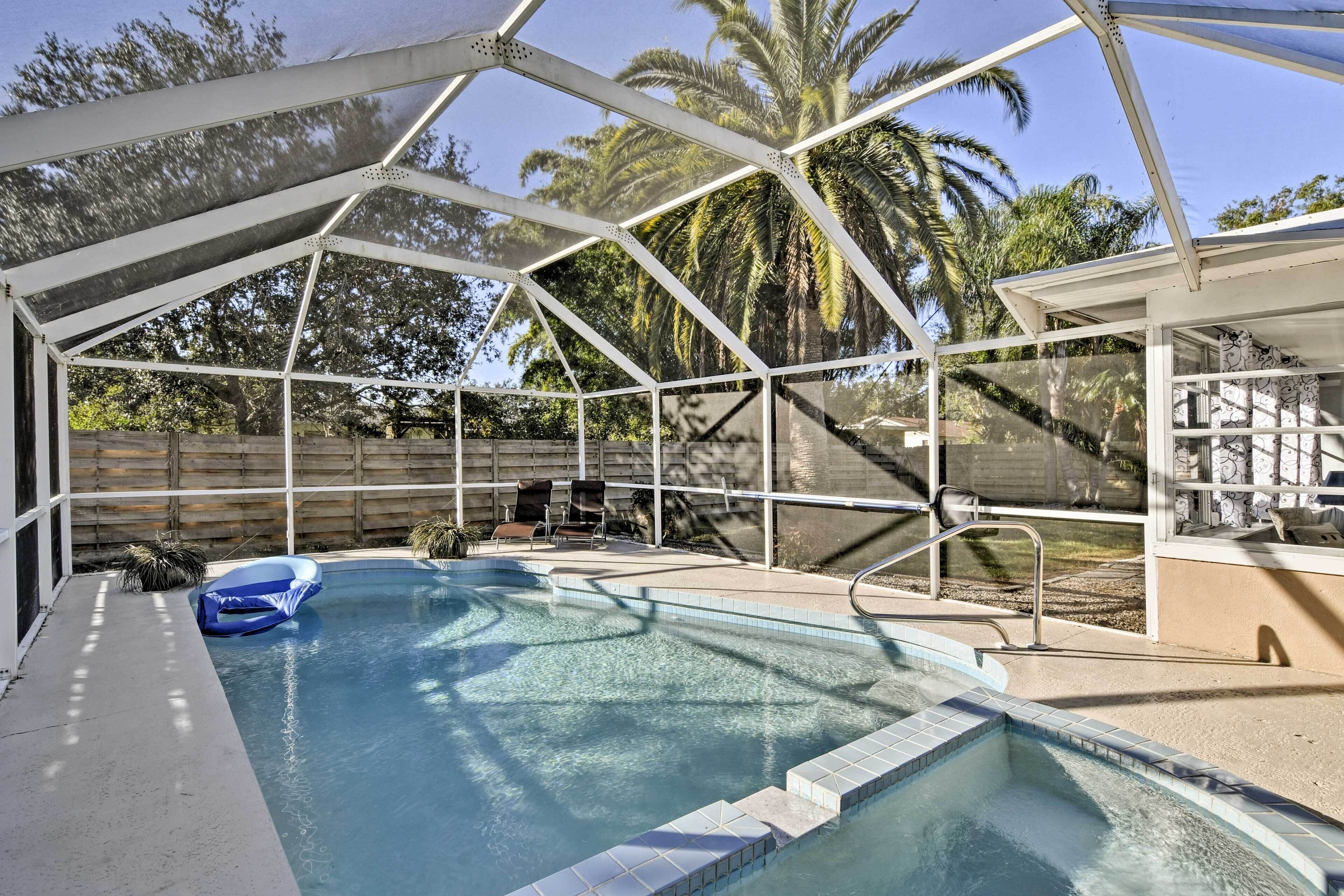 A covered swimming pool with a clear view of the surrounding area, including a wooden fence and palm trees.