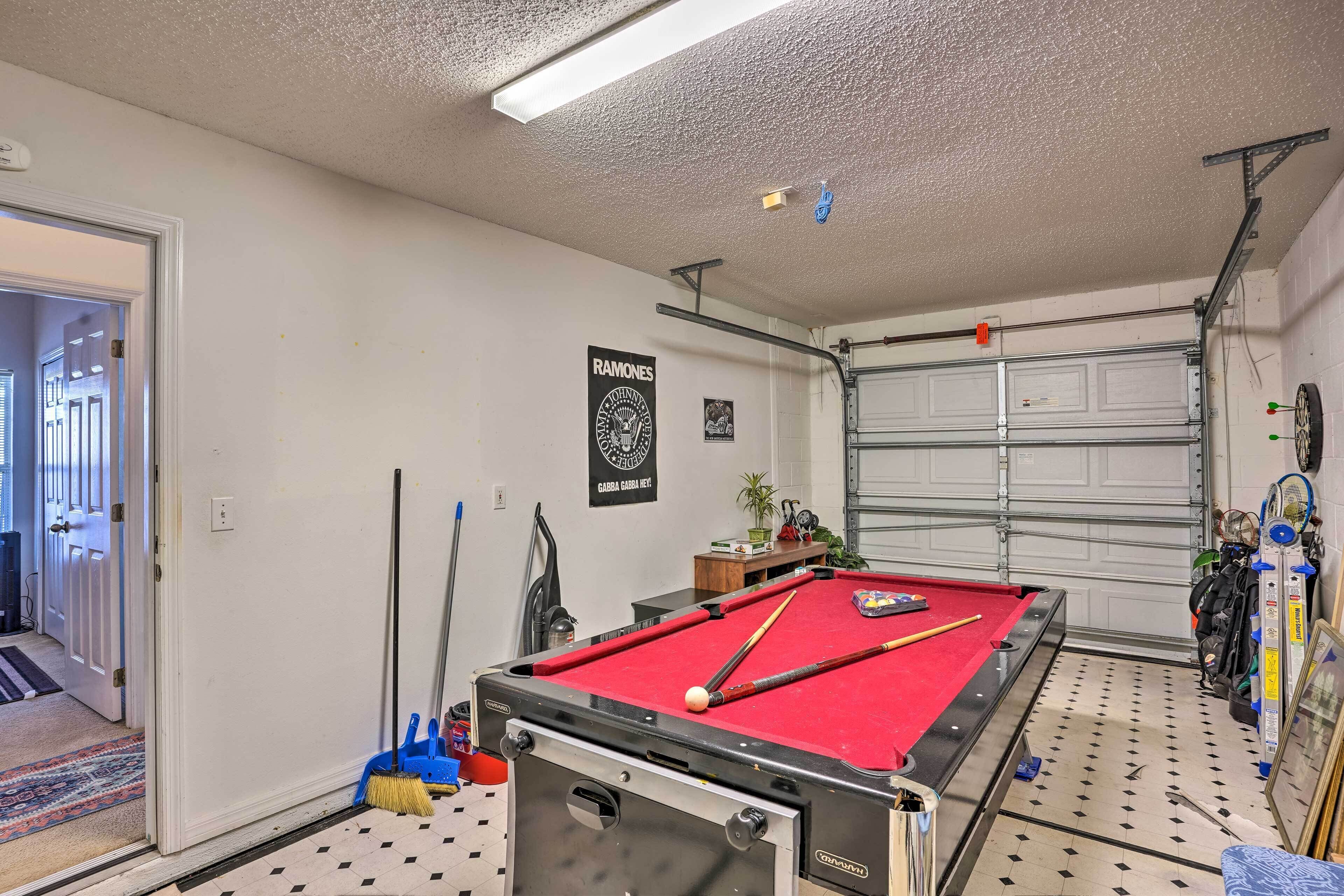 A pool table in a room with a garage door, a broom, and a vacuum cleaner.
