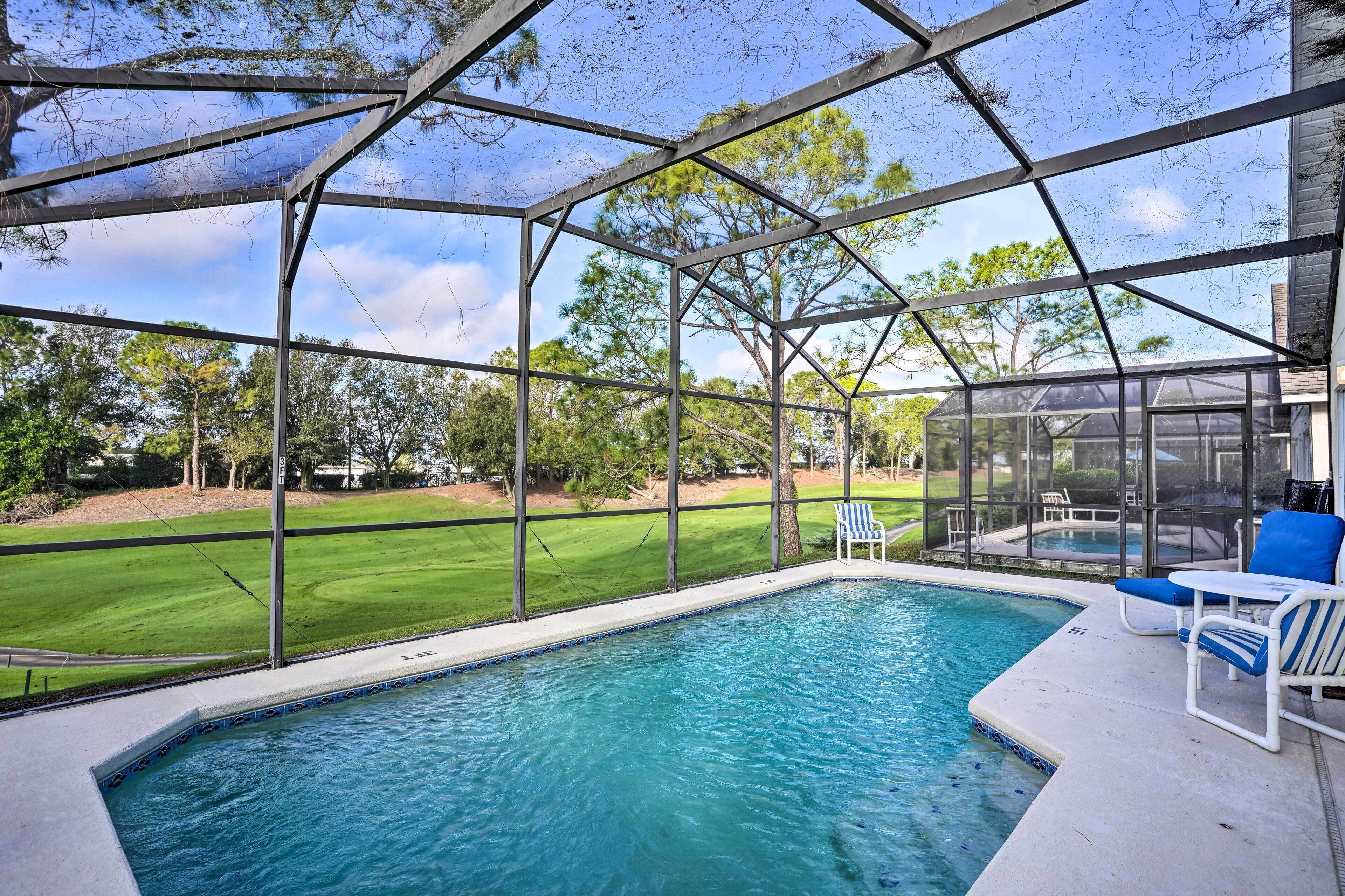 A covered swimming pool with a view of a green lawn and trees.