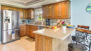 A kitchen with wooden cabinets, stainless steel appliances, a granite countertop, and a bar area with stools. - Lanai, Pool & Hot Tub! Fort Myers Extended Stay (Fort Myers)