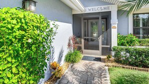 A building entrance with a 'WELCOME' sign, a door, and a small garden area with plants and a pathway. - Lanai, Pool & Hot Tub! Fort Myers Extended Stay (Fort Myers)