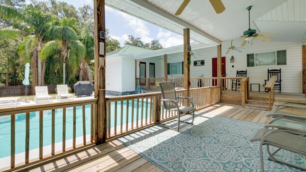 Et poolområde med træterrasse, liggestole, en pool og en overdækket patio med ventilatorer.