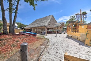 A beachside area with a thatched-roof building, a wooden ship, and a fenced area with a trash can. - Pool Access: Homosassa Home Near Boat Launch! (Homosassa)