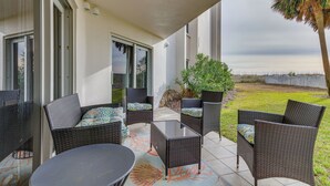 Un espace extérieur aménagé en terrasse, avec des meubles en osier, une table en verre et une vue sur la pelouse et les palmiers.
