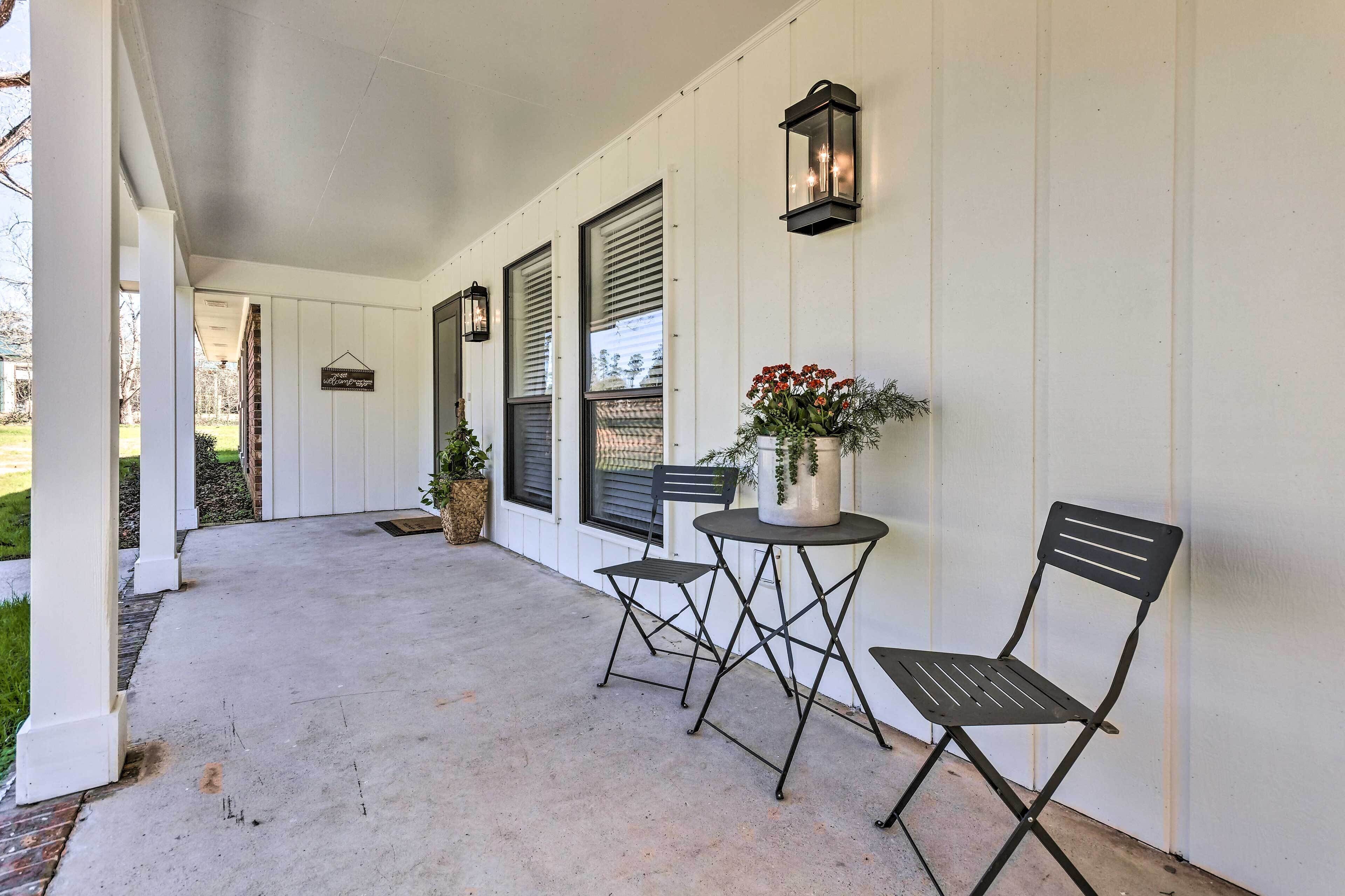 A covered porch with two metal chairs and a small table, a potted plant, and a wall-mounted lantern.